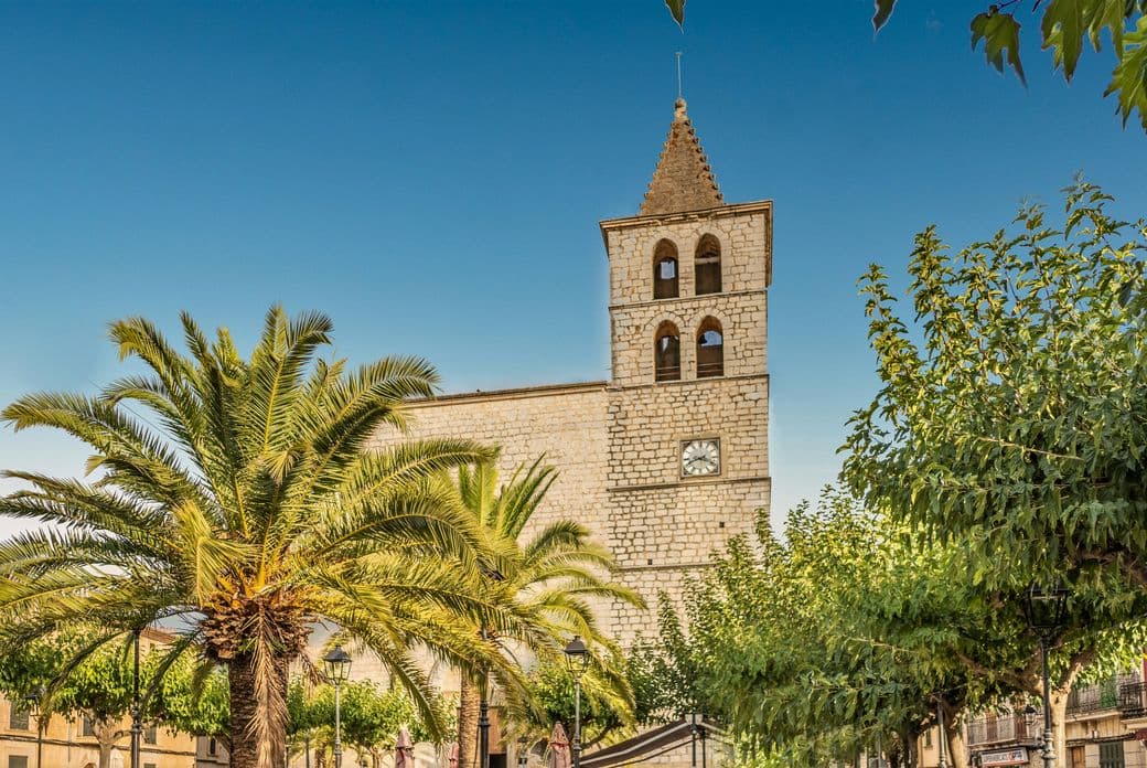 "View of the main square in the interior Majorcan village of Campanet, surrounded by traditional stone buildings and shaded by trees