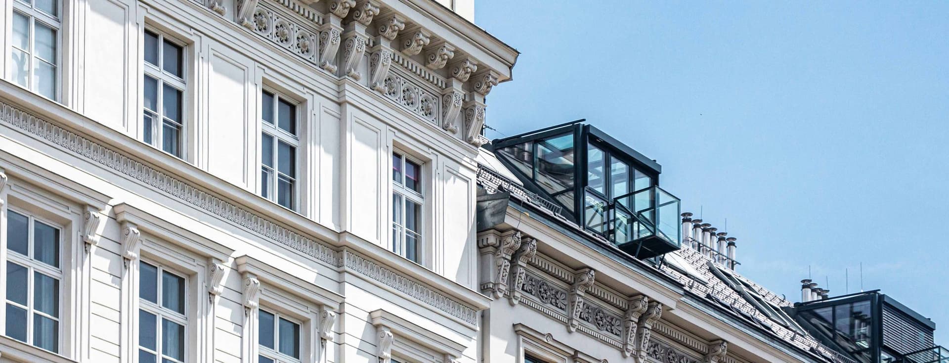 Historische weiße Gebäude mit verschnörkelten Fassaden und modernen Glasdächern unter einem klaren blauen Himmel.
