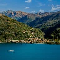 Veduta panoramica di Varese dal lago: il profilo della città immerso nel verde, con colline sullo sfondo e riflessi sull’acqua in una giornata luminosa.