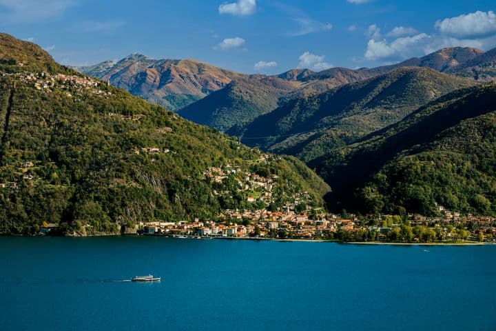 Veduta panoramica di Varese dal lago: il profilo della città immerso nel verde, con colline sullo sfondo e riflessi sull’acqua in una giornata luminosa.