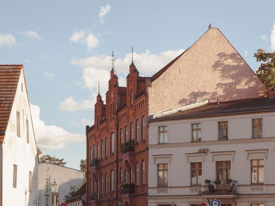 Historic red brick building with ornate spires beside a white building under a clear blue sky with scattered clouds.