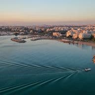 Aerial view of a boat moving on blue water near a city at sunset.