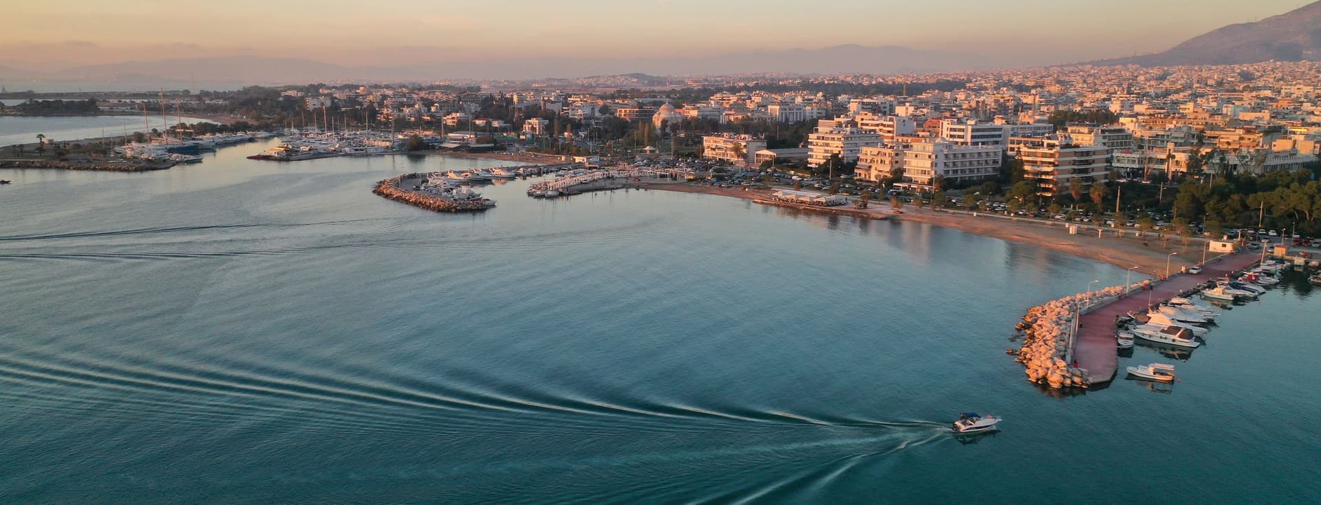 Aerial view of a boat moving on blue water near a city at sunset.