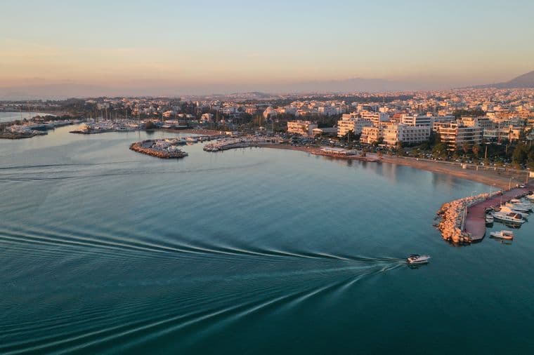 Aerial view of a boat moving on blue water near a city at sunset.