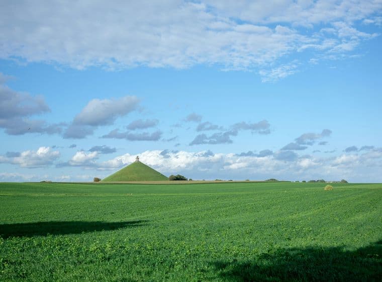 Groen veld met een kegelvormige heuvel op de achtergrond onder een blauwe lucht met witte wolken.