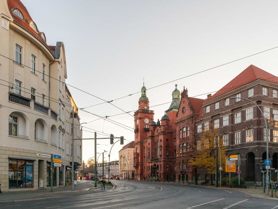 Street view of an intersection with historic buildings, including a red-brick structure with towers, under a clear sky at sunset.