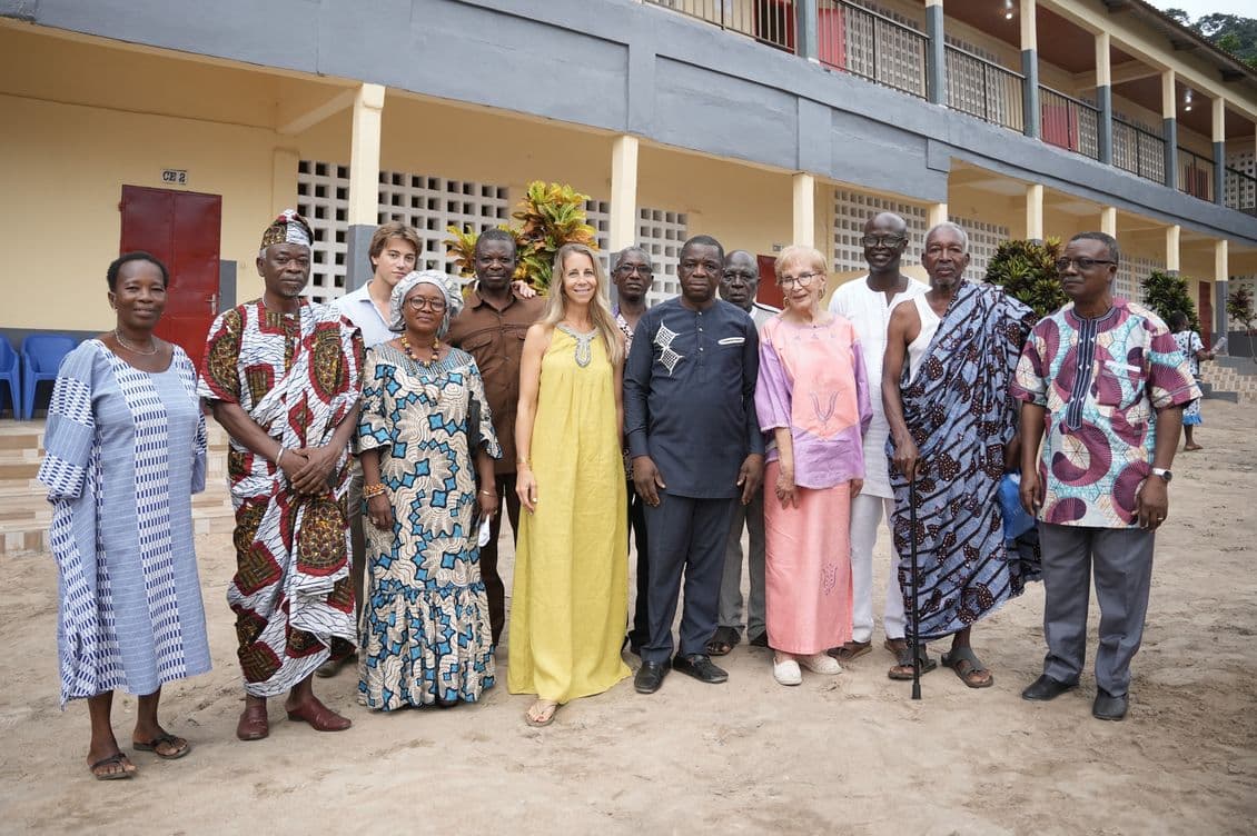 A diverse group of people stands smiling in front of a large building with multiple balconies.