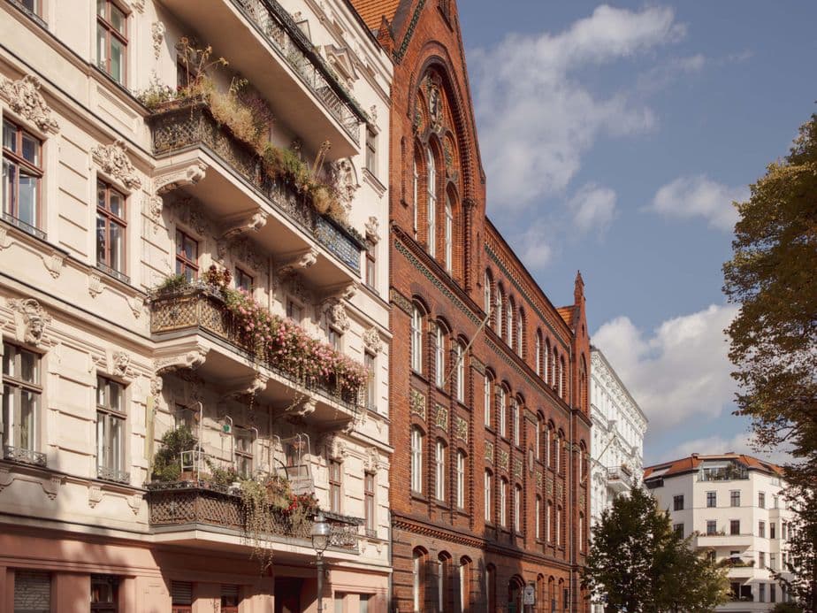 Historic European street with ornate balconies, red brick and white buildings, under a clear blue sky.