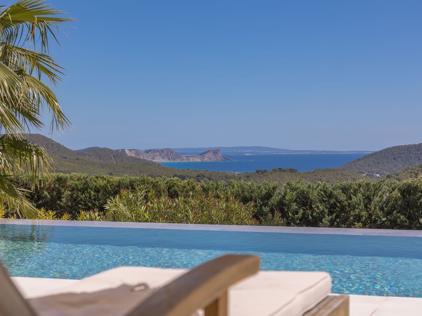 Wunderschöne Terrasse auf Ibiza mit einem ruhigen Pool, der einen traumhaften Blick auf grüne Hügel und die Mittelmeerküste in der Ferne bietet – der perfekte Ort, um inmitten der Natur zu entspannen.