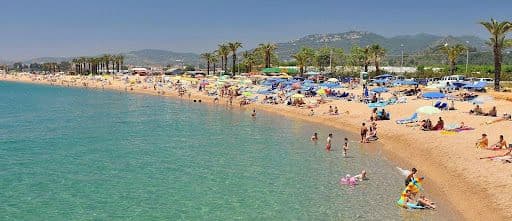 Playa muy larga con muchas personas bañándose o tomando el sol