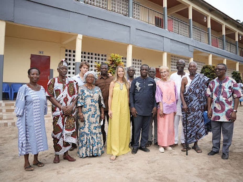A diverse group of people stands together smiling in front of a large building with multiple balconies.