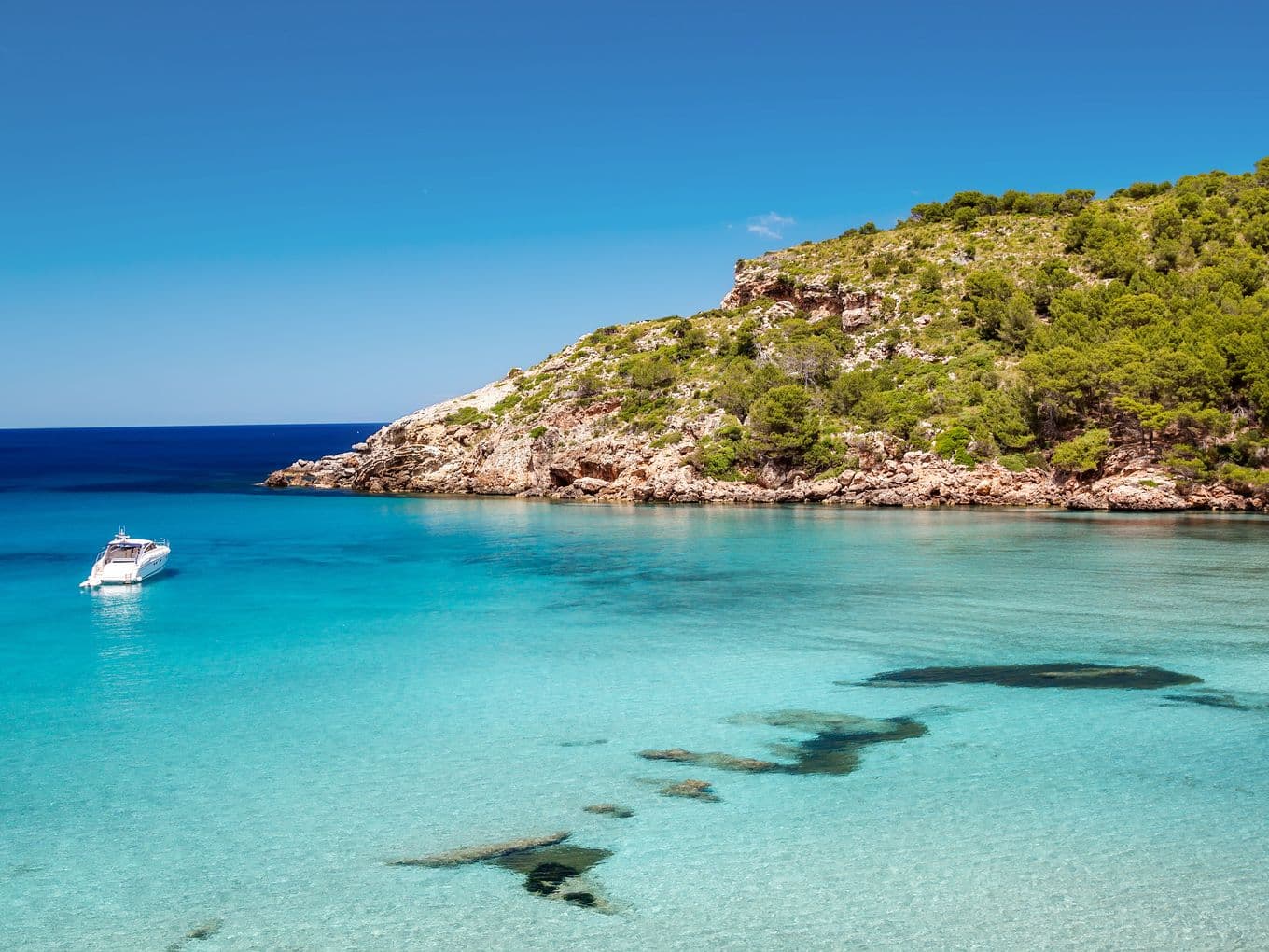 Impresionante vista de una cala apartada en Menorca con aguas turquesas y cristalinas, arenas blancas y un entorno natural rocoso: un auténtico paraíso mediterráneo.