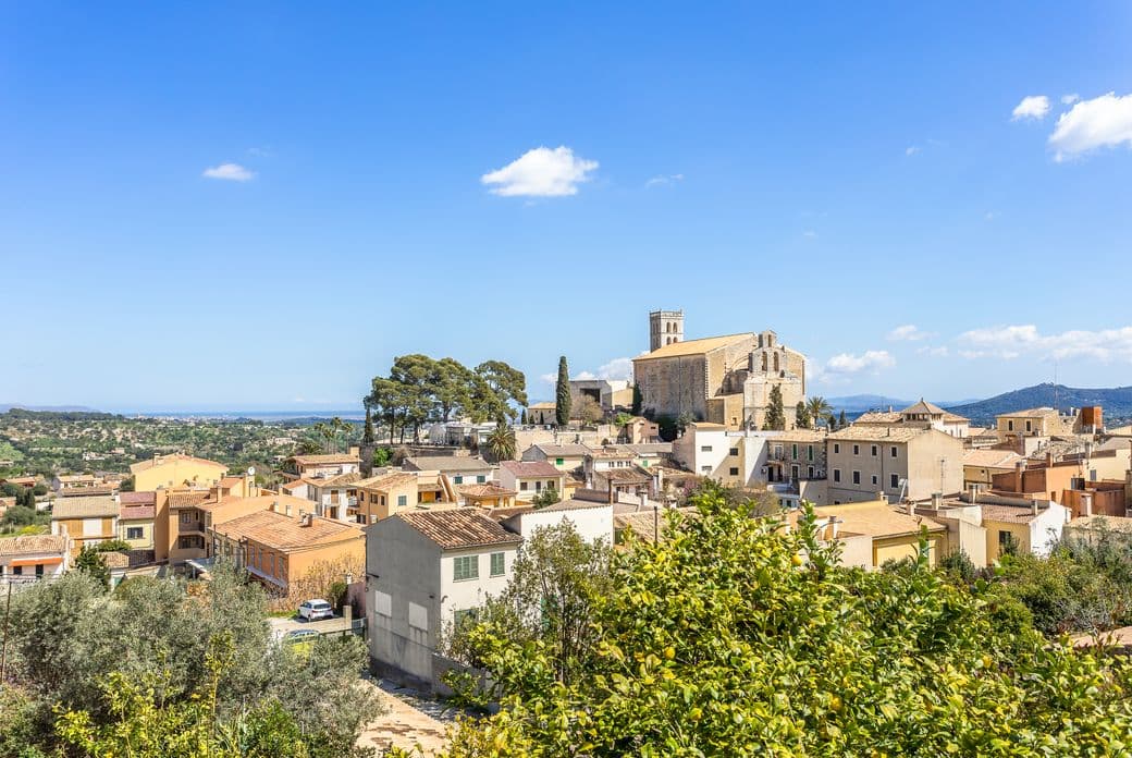 Vista panoràmica sobre els teulats de Selva, Mallorca, amb l'església del poble elevant-se al fons contra un cel blau.