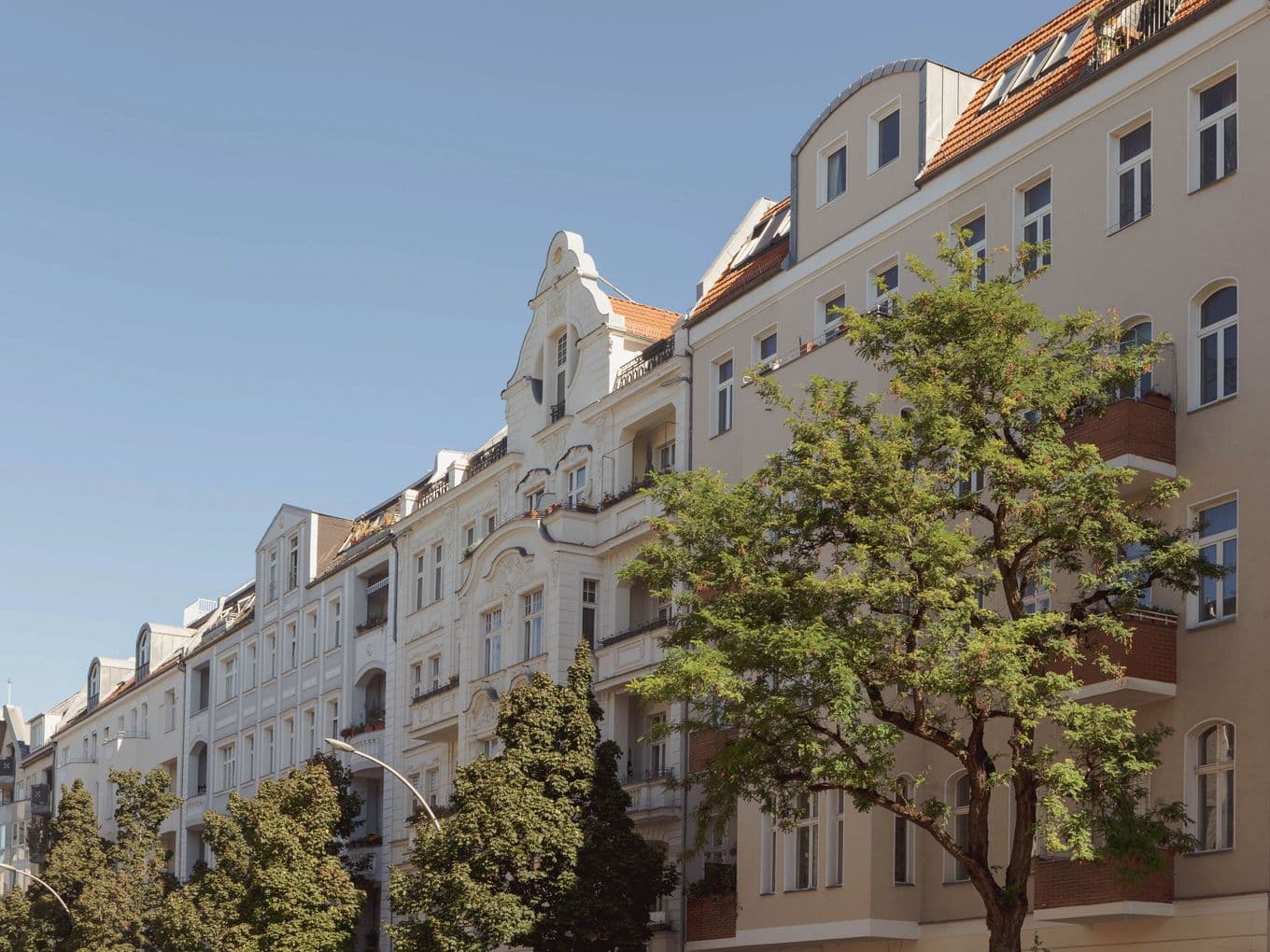 Street view of elegant European-style apartment buildings with ornate facades and a tree-lined sidewalk under a clear blue sky.