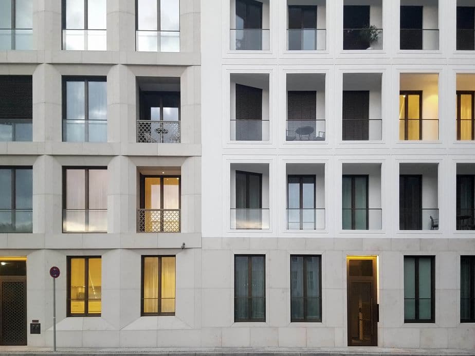 Modern building facade with a grid of windows. The left side has a grey tone, and the right side is white, with some lit interiors.