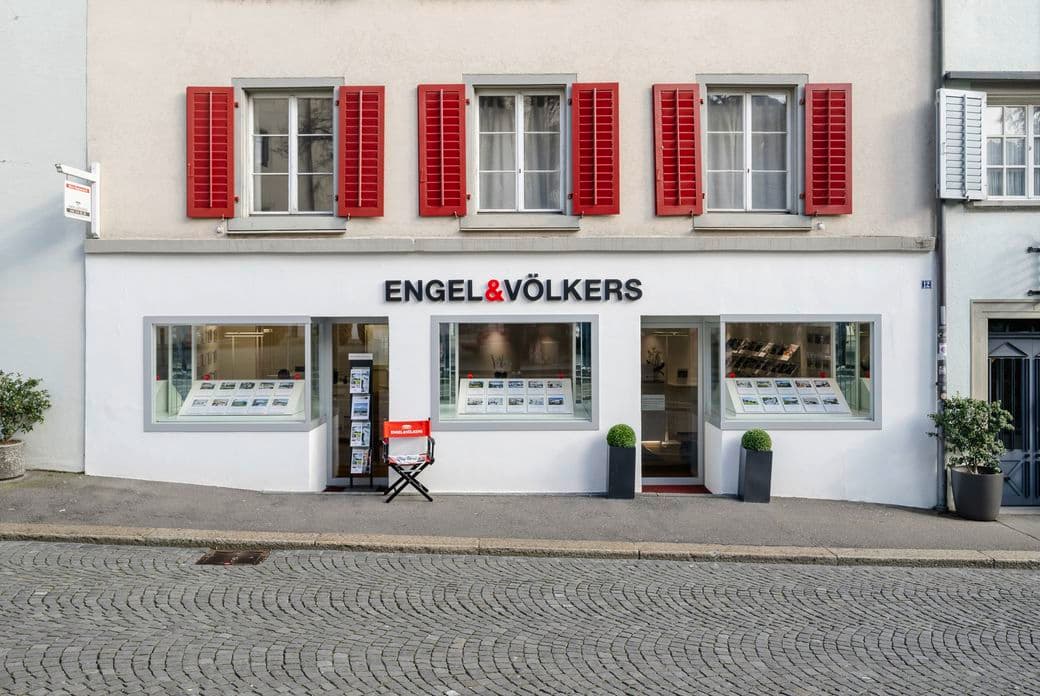 Exterior view of the Engel & Völkers shop in Rapperswil. Large Engel & Völkers logo, plus two box trees in front of the entrance door.