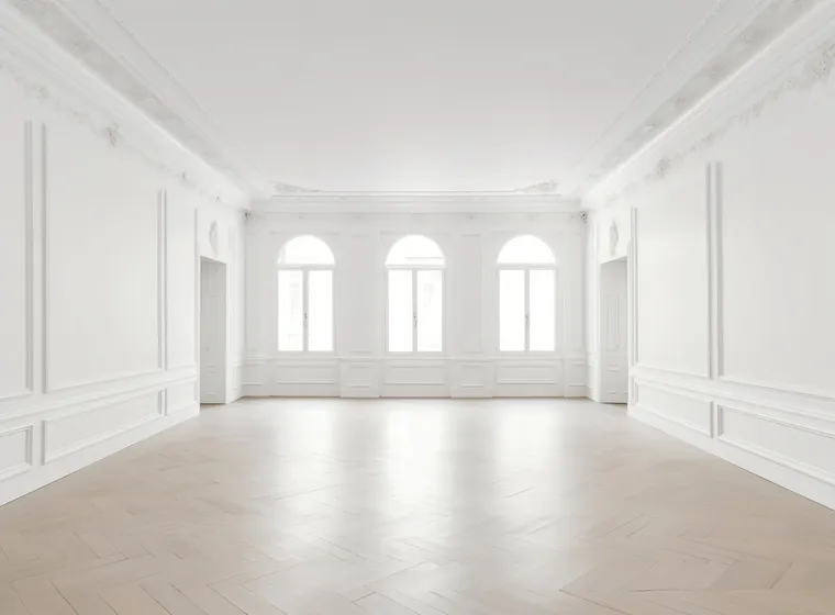 Bright and airy room featuring decorative moldings on the walls and ceiling, large arched windows in the background, and light herringbone parquet flooring.