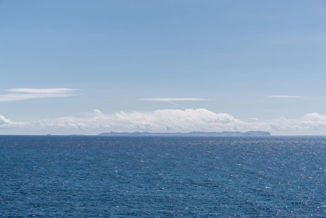 Penya-segats rocosos i aigües turqueses a Cala Pi, Mallorca, amb l'illa de Cabrera a l'horitzó.