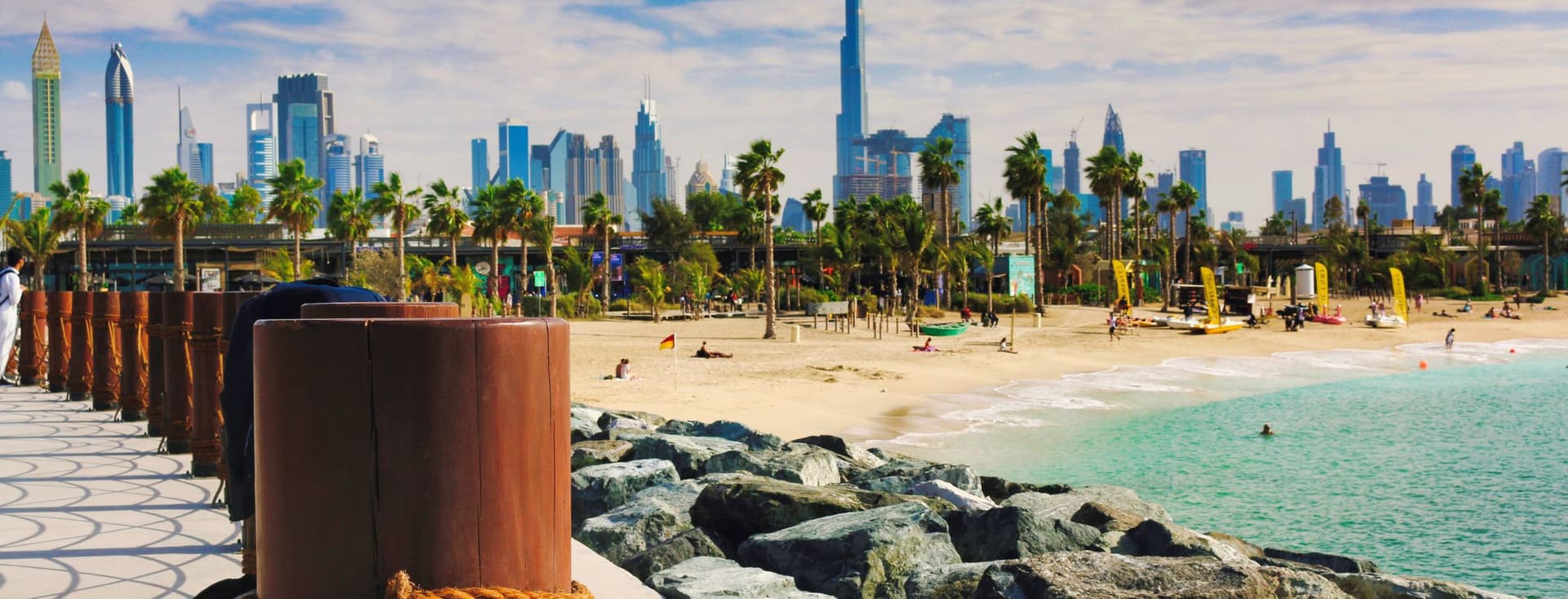 Ein malerischer Blick auf einen Sandstrand mit der Skyline von Dubai im Hintergrund, der wichtige Faktoren wie Leben am Wasser und Stadtnähe bei der Standortwahl in Dubai darstellt.