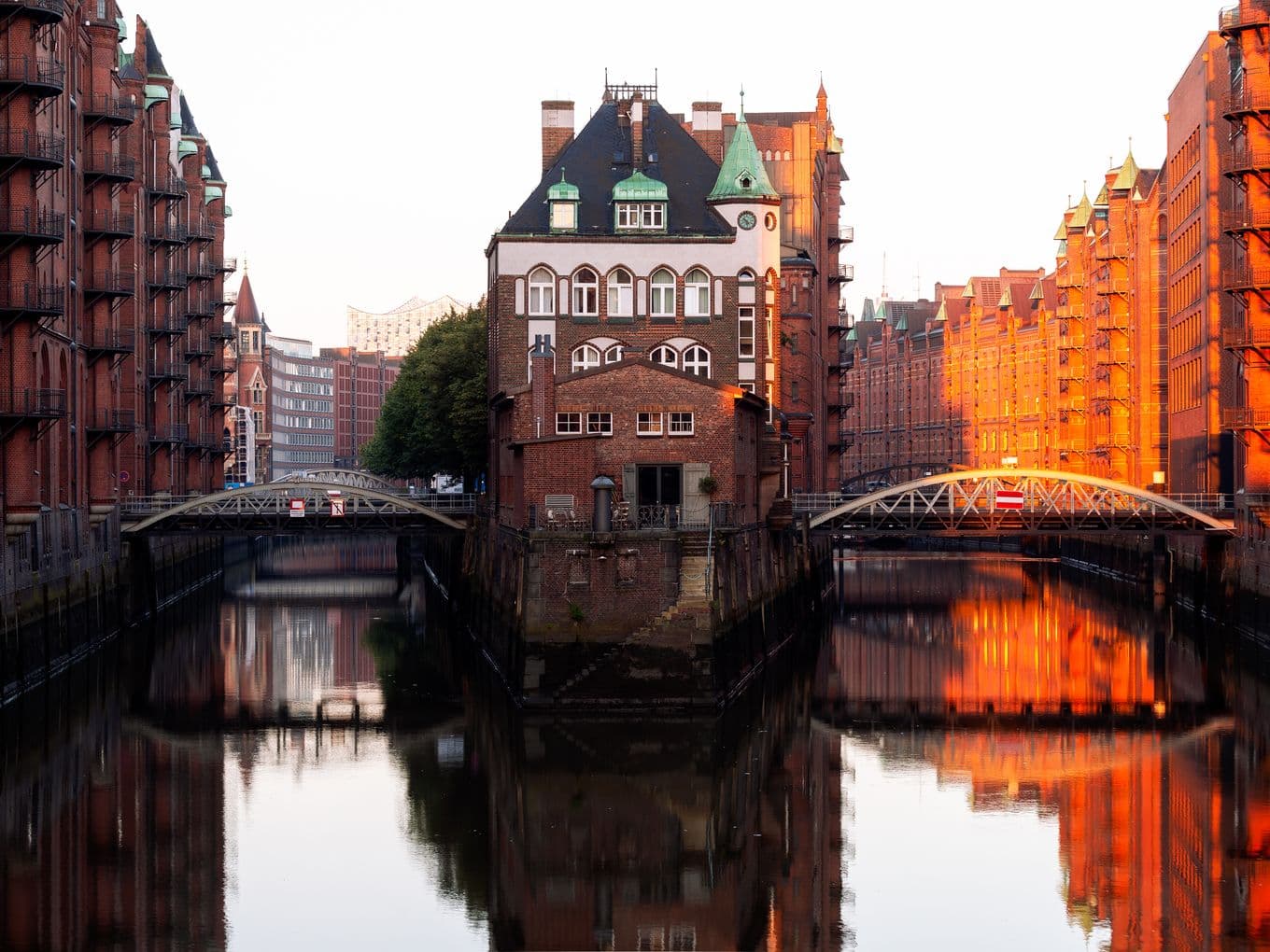 Historic brick building between canals in HafenCity, Hamburg, reflected in the water while warm sunlight illuminates the scene.