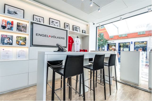 Engel & Völkers office interior with a white desk, black chairs, and a view of a European street through a large window.