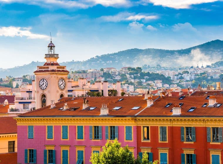 Tour de l'horloge et bâtiments colorés à Nice, France. Bâtiments roses et rouges avec des volets bleus. Montagnes en arrière-plan.