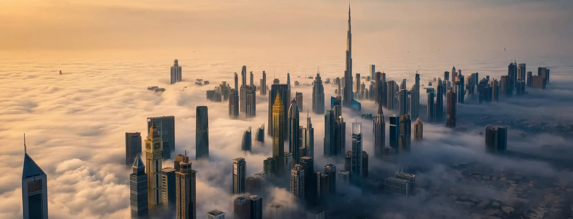 Aerial view of a cityscape with skyscrapers piercing through clouds, bathed in golden sunlight at dawn.