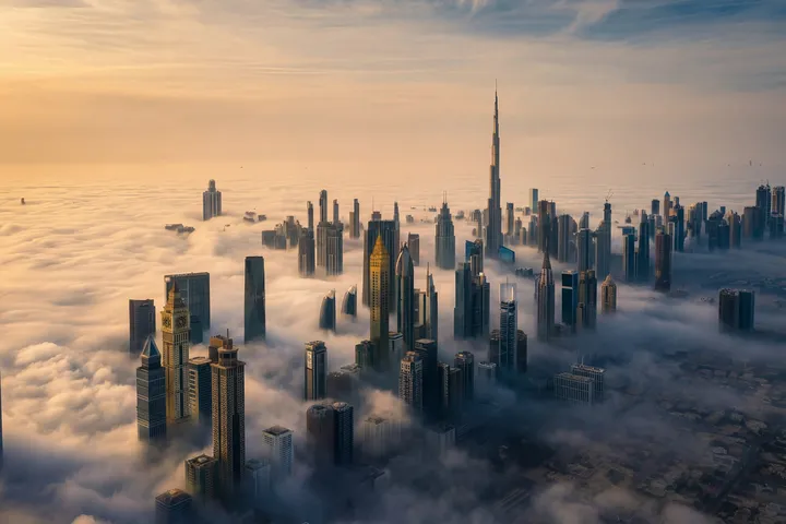 Aerial view of a cityscape with skyscrapers piercing through clouds, bathed in golden sunlight at dawn.