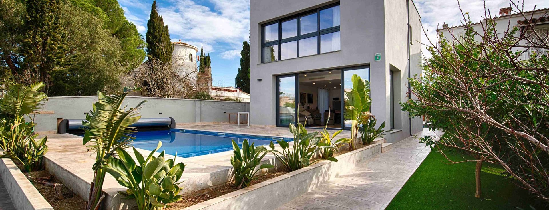 View of a modern house with swimming pool at its entrance, garden around it and blue skies with clouds