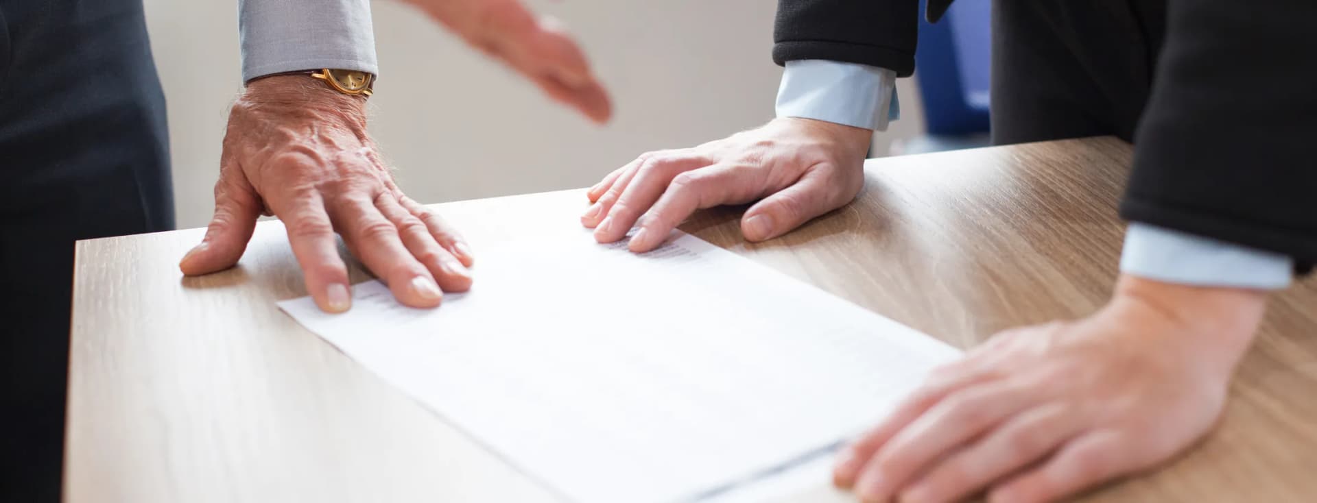 devi solo tradurre Zwei Personen beugen sich über einen Holztisch mit einem Dokument. Eine Person legt eine Hand auf das Blatt, während die andere danach greift. KI-generiertes Bild