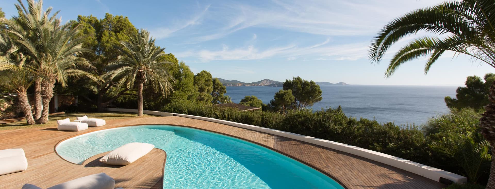 Ein Pool mit Palmen, mit Blick auf das Meer und die Berge.