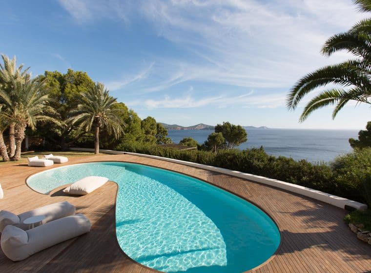 Ein Pool mit Palmen, mit Blick auf das Meer und die Berge.