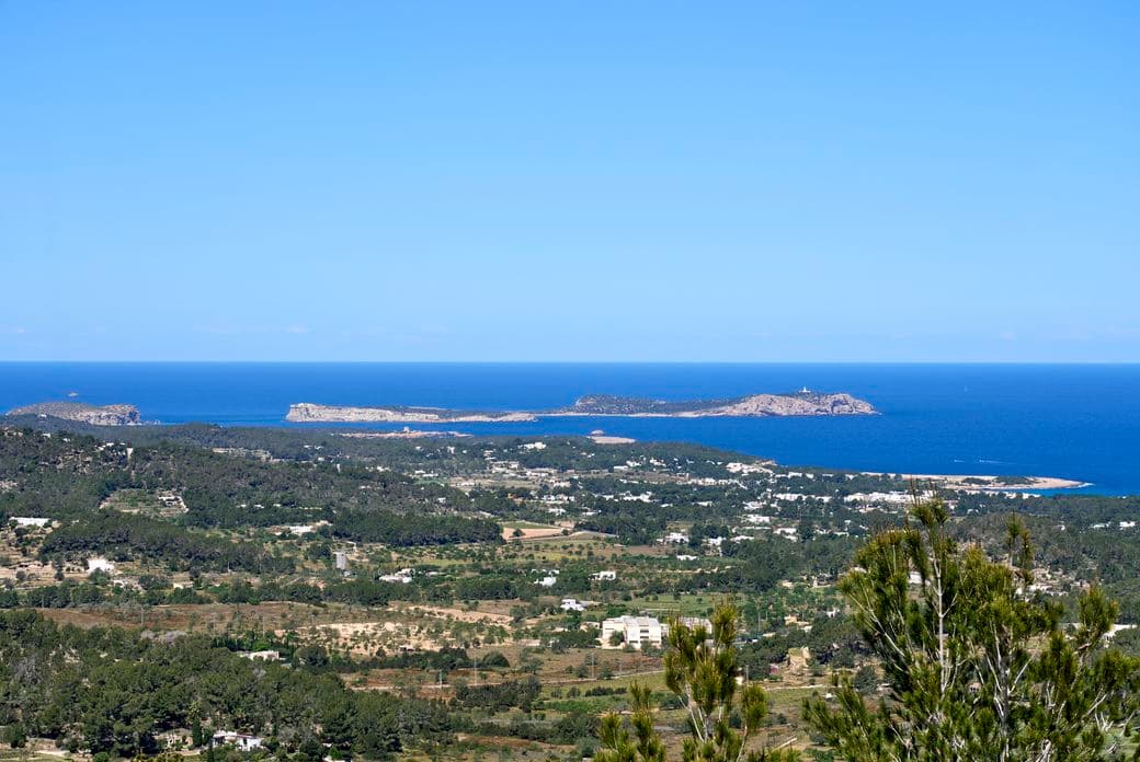 Malerischer Ausblick von einem Küstenpanorama in Ibiza – mit weitem Blick über das Mittelmeer und der ruhigen Silhouette der Insel Sa Conillera am Horizont.