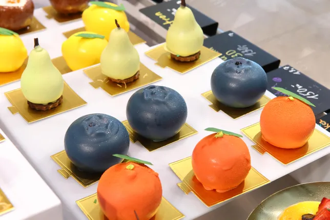 A selection of carefully shaped desserts resembling pears, blueberries and citrus fruits, displayed on golden bases.
