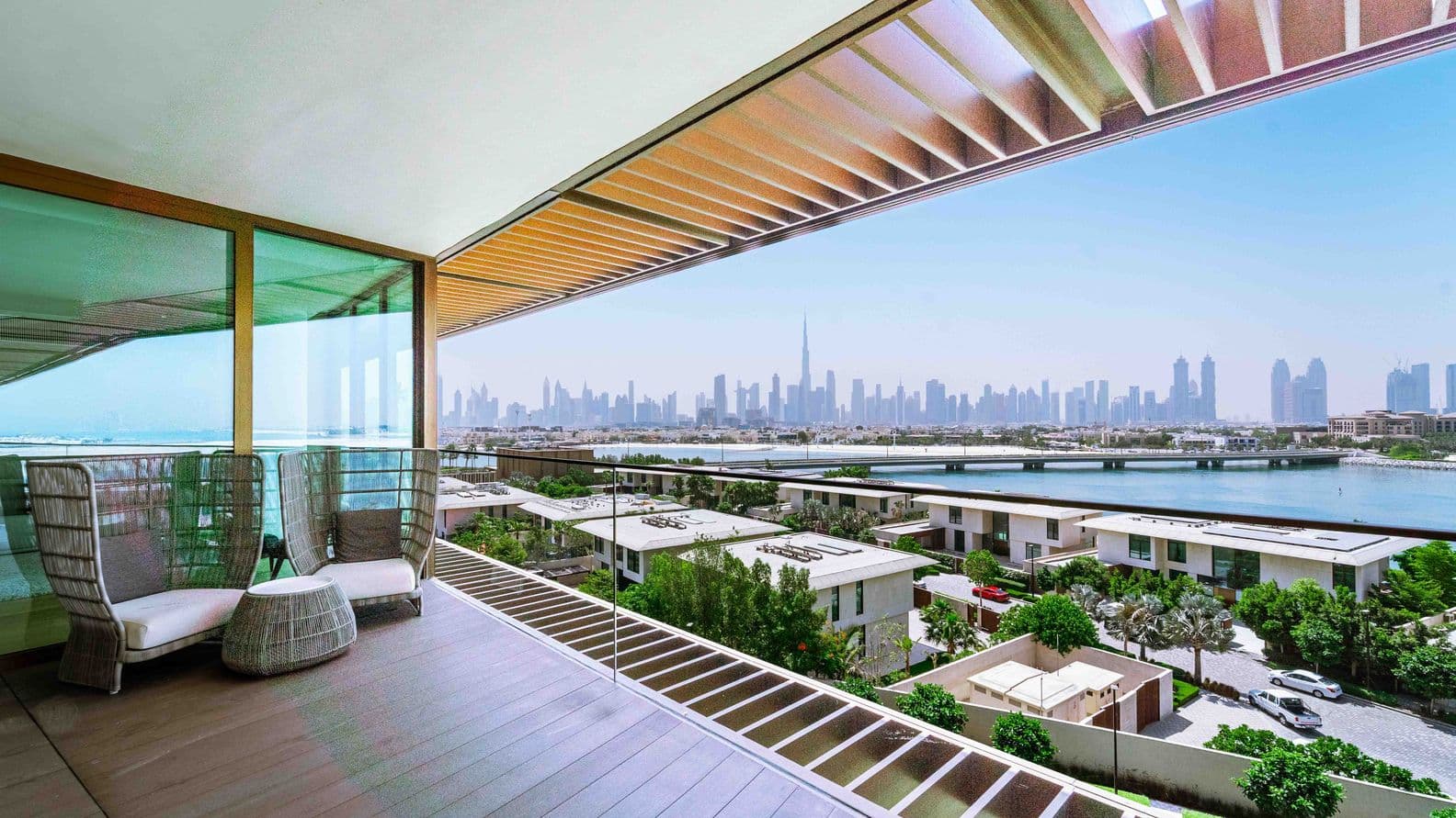 Spacious balcony with seating, overlooking a cityscape with a prominent skyline and water view under a clear blue sky.