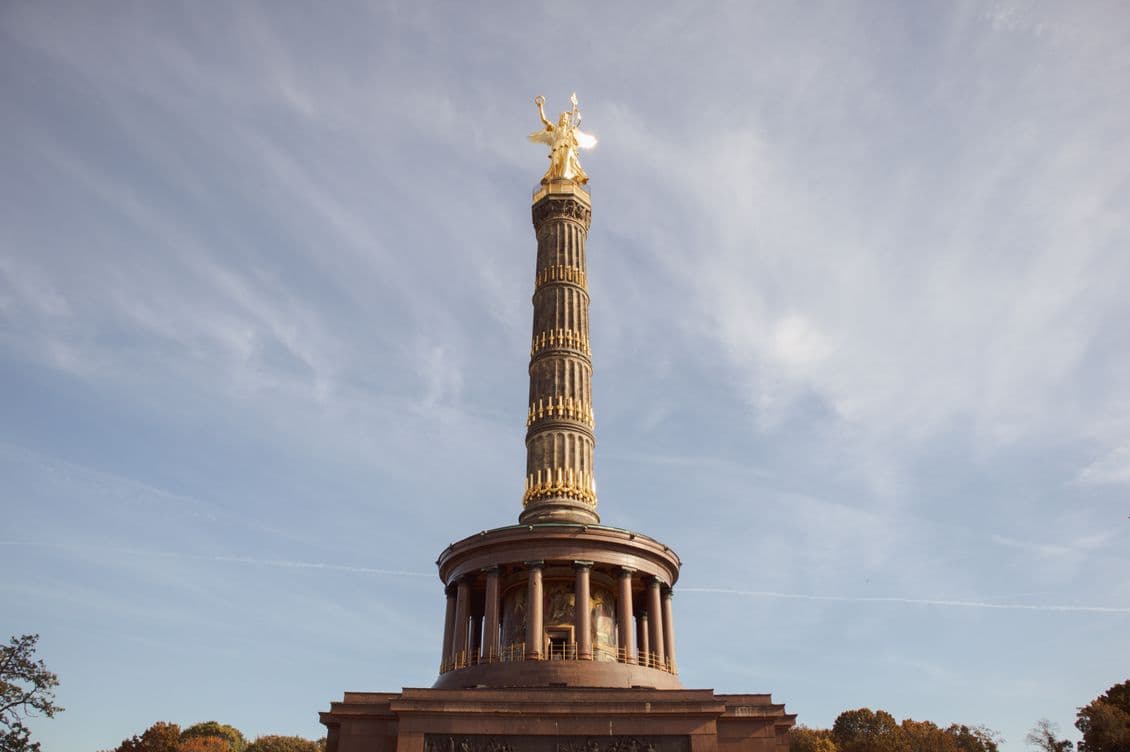 The Berlin Victory Column with a golden statue atop, set against a partly cloudy sky.