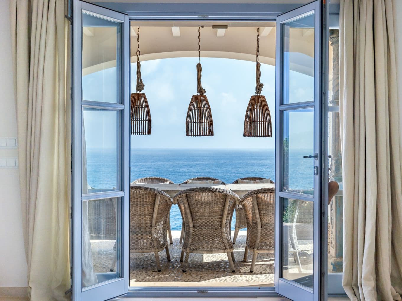 View from inside a house in Cala Murada, looking out onto a beautiful terrace with the shimmering sea visible in the distance