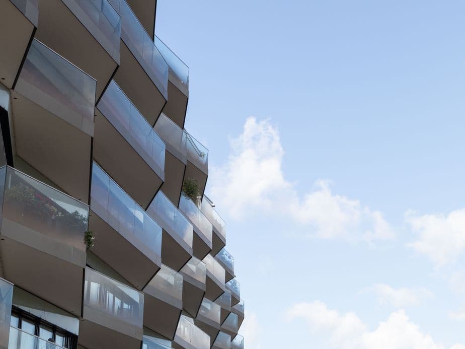 Modern building with glass balconies on the left, set against a clear blue sky with scattered clouds on the right.