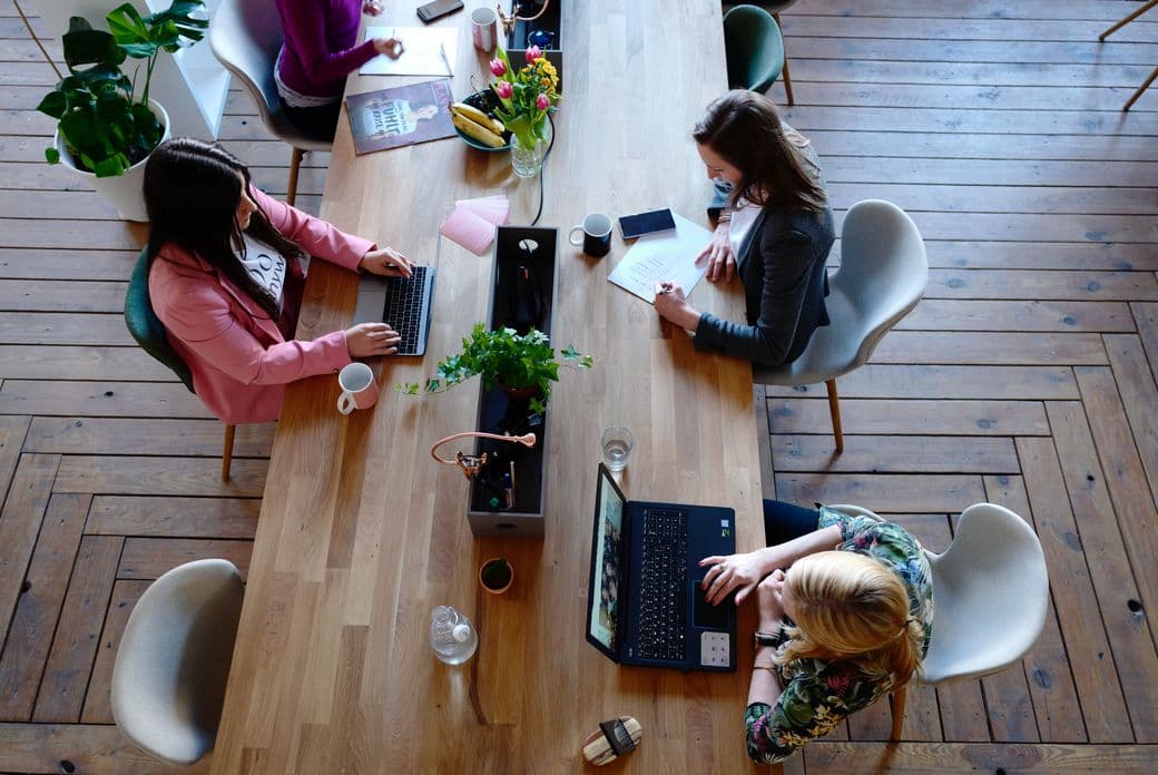 3 women coworking at big wooden table from bird perspective