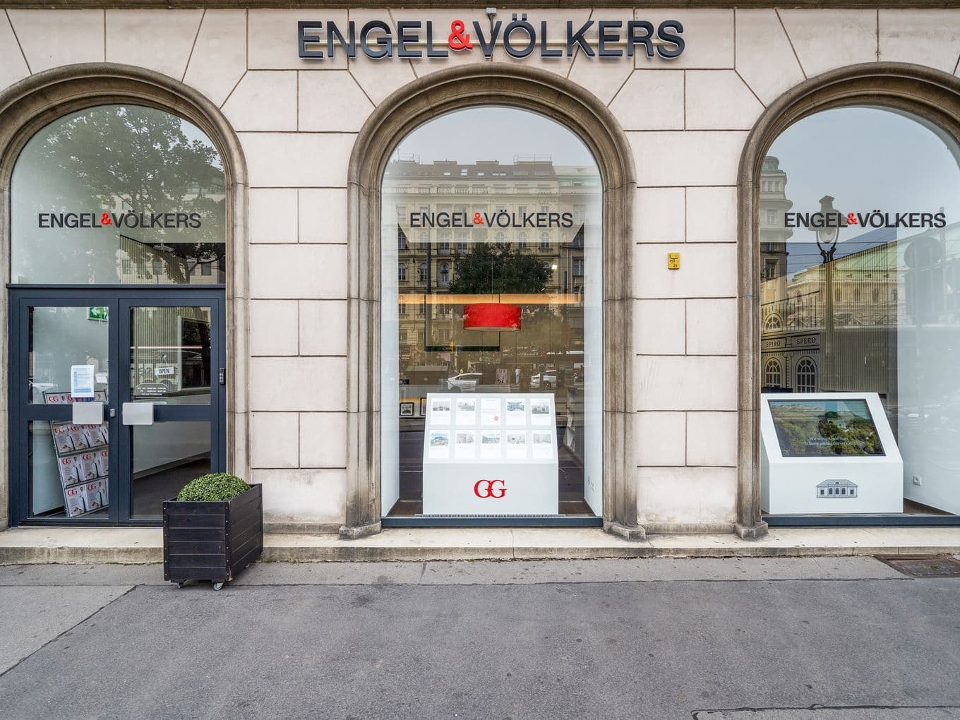 Storefront of Engel & Völkers with three large arched windows, displaying real estate listings outside.