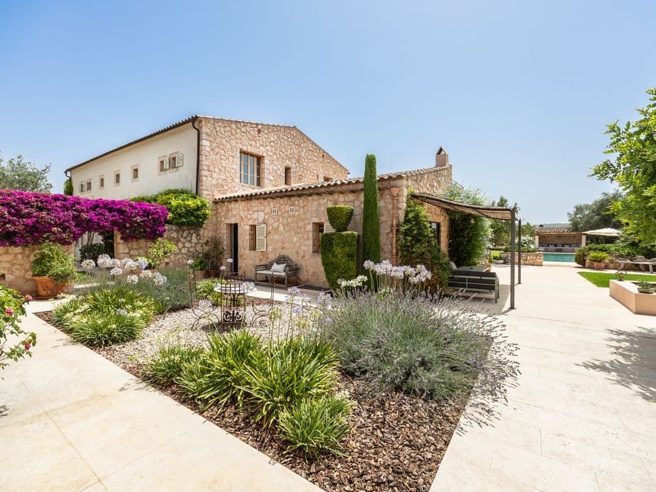 Preciós pati d'una finca mediterrània a Santa Maria, amb parets de pedra rústiques, plantes en testos, portes amb arc i una atmosfera tranquil·la i assolellada.