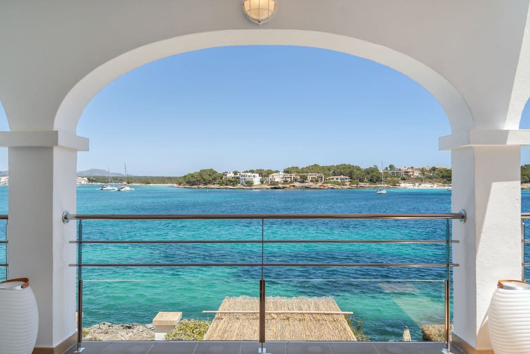 Scenic view from a terrace overlooking the picturesque harbour of Portocolom, with calm waters, moored boats, and charming coastal surroundings