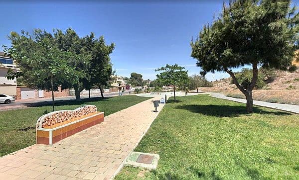 A park with an orange bench, trees, grass, and a blue sky can be seen.