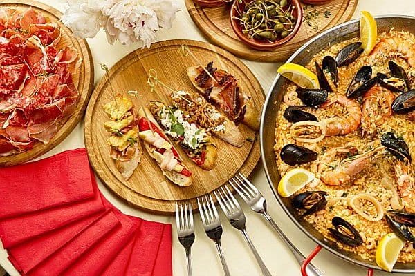 Mostra un plat típic de paella de marisc en un restaurant, així com unes tapes i un plat amb pernil i altres embotits.