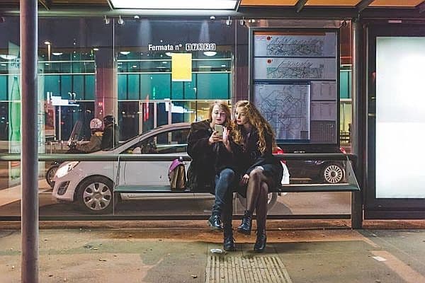 Foto de dues noies assegudes fora de l'aeroport utilitzant l'app d'autobús per a la línia Costa Azul.