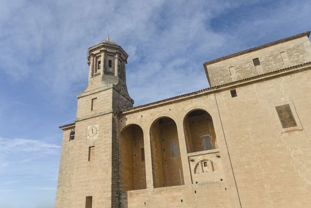 Façana de pedra i campanar de l’Església de Sant Miquel a Llucmajor sota un cel blau clar.