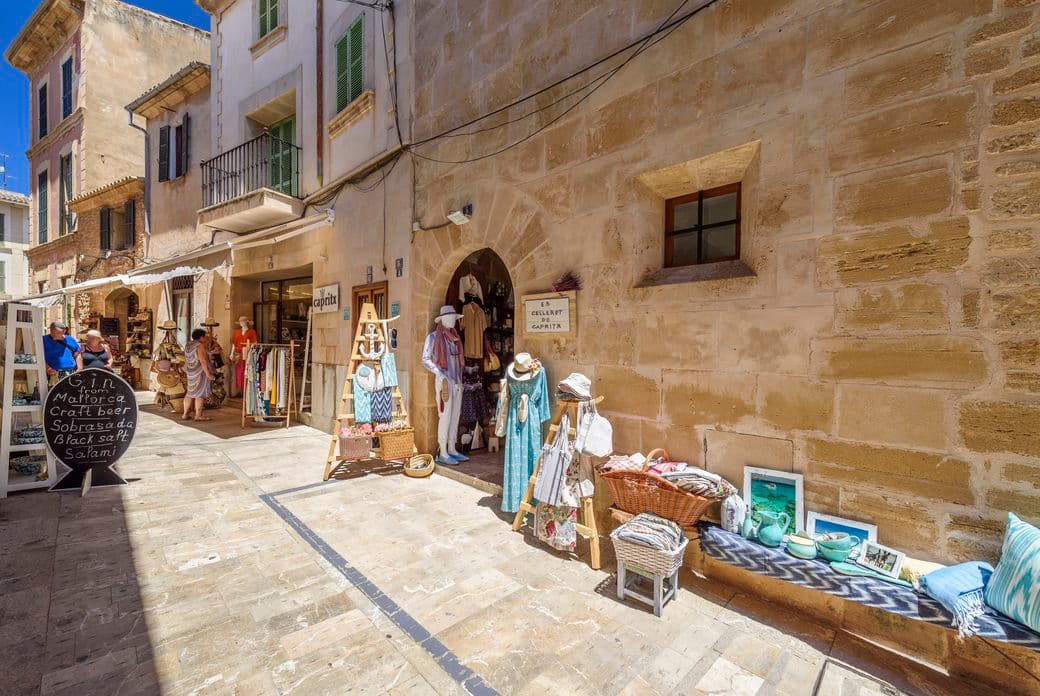 Una animada calle comercial en el casco histórico de Alcudia, rodeada de tiendas locales y arquitectura tradicional.
