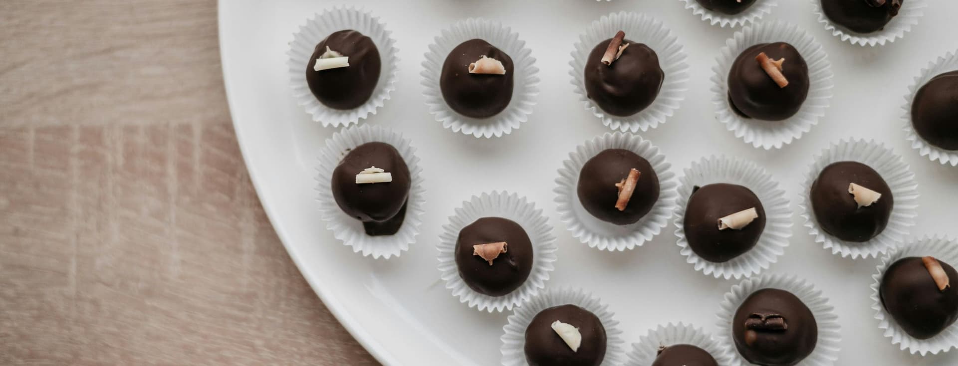 Des truffes au chocolat sur une assiette blanche. Chaque truffe est dans un moule en papier blanc et surmontée d'une spirale de chocolat. L'assiette est posée sur une surface en bois marron clair.