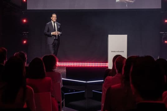 Till Fabian Zalewski, CEO di Engel & Völkers DACH, tiene un discorso su un palcoscenico di fronte a un pubblico e a un podio in bianco