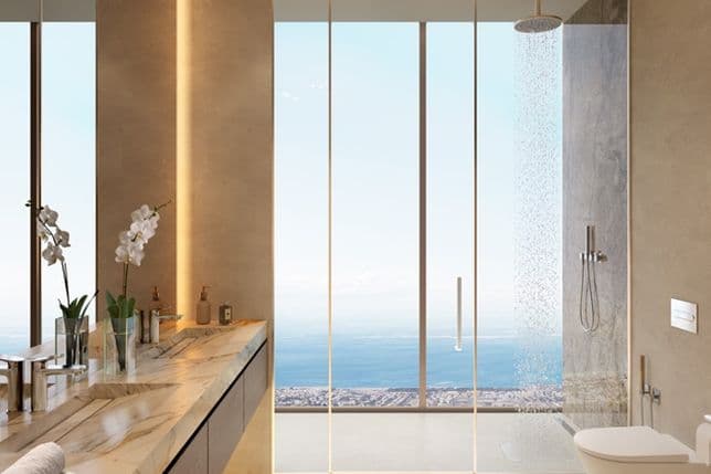Modern bathroom with marble countertop, orchids, and a glass shower overlooking the ocean. Floor-to-ceiling windows enhance the panoramic view.